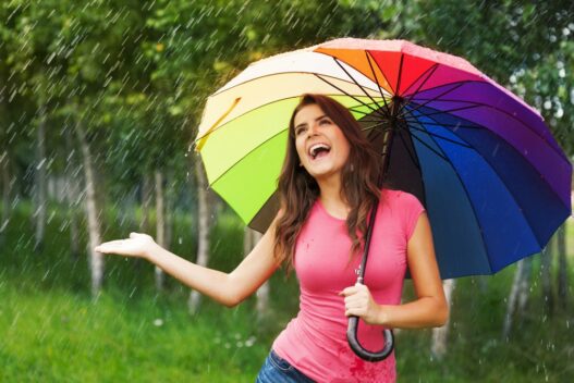 Kvinde med paraply i regnvejr i sin have